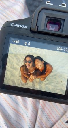 a person holding up a camera with two women on the beach in front of them