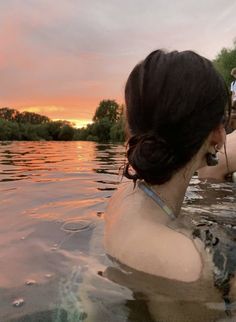 a woman is swimming in the water with her hair pulled back into a bun at sunset