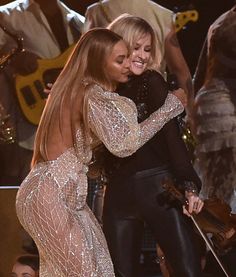 two women hugging each other on stage at an awards show with musicians in the background