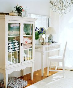 a white china cabinet sitting in the corner of a room next to a table and chair