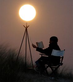 a person sitting in a chair reading a book under a bright light on top of a hill