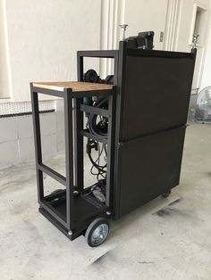 a black cart sitting inside of a building next to a white wall with windows on it