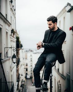 a man sitting on top of a building while looking at his cell phone