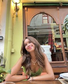 a beautiful young woman sitting at a table in front of a store window smiling for the camera