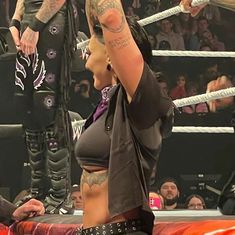 a woman with tattoos on her arm standing next to a wrestling ring