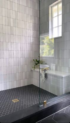a white tiled bathroom with a glass shower door and black tile flooring on the walls