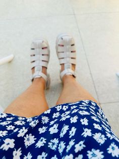 a woman's legs with white shoes and blue floral print dress on the ground