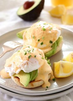 eggs benedict with avocado and sour cream sauce on a plate next to sliced lemons