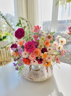 a vase filled with lots of colorful flowers on top of a white table next to a window