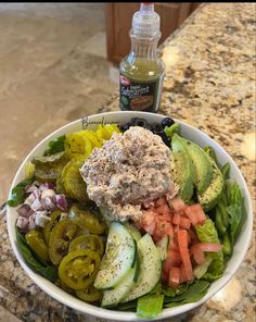 a salad with dressing in a bowl on the counter next to a bottle of ketchup