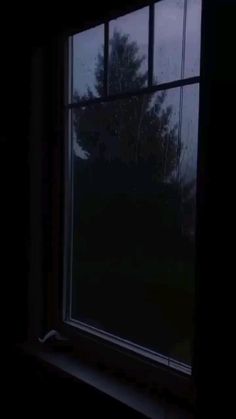 a dark room with a large window and trees outside the window at night, looking out