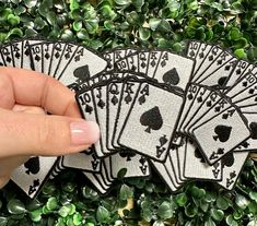 a hand holding four playing cards in front of some green plants