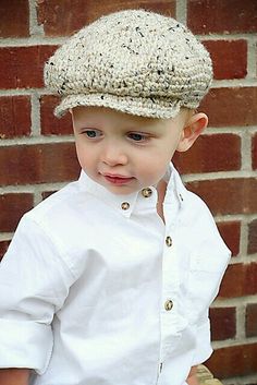 a young boy wearing a white shirt and a crocheted hat is standing in front of a brick wall