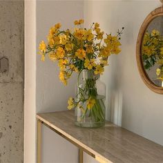 yellow flowers sit in a vase on a shelf next to a mirror and light fixture