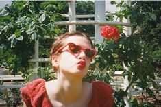 a woman wearing red sunglasses in front of a rose bush