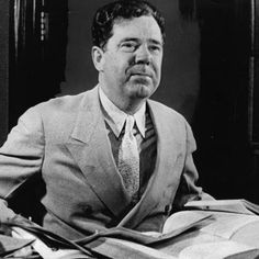 a man in a suit and tie sitting at a desk with papers on it, looking off to the side