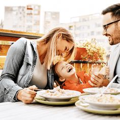 a man and woman sitting at a table eating food with a baby in front of them