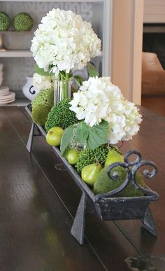 flowers and fruit are arranged in a wagon on the dining room table, along with other decorations