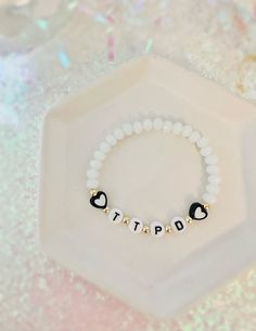 a white beaded bracelet with black and gold beads that says tripp on it