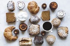 a table topped with lots of different types of pastries next to a cup of coffee
