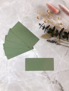 some green cards sitting on top of a white table next to dried flowers and plants