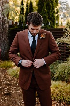 a man in a brown suit and tie is looking down at his pocket while wearing a flower boutonniere