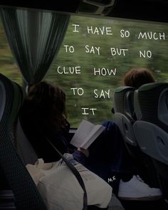 two people sitting on a bus looking out the window with an open book in their lap