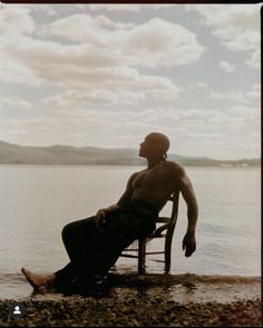a man sitting in a chair on the beach next to the water with his eyes closed
