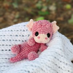 a small pink teddy bear sitting on top of a white knitted blanket with black eyes