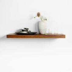 a white vase sitting on top of a wooden shelf next to glasses and plates in front of a white wall