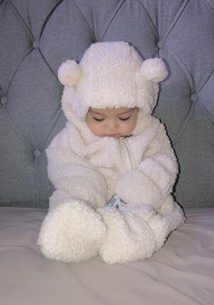 a small child wearing a white teddy bear costume sitting on a bed with his hands in his pockets