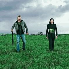 two men are walking through the grass in front of an overcast sky