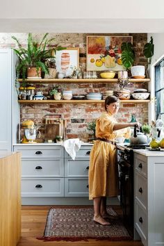 a woman standing in a kitchen preparing food on top of a stove next to a brick wall