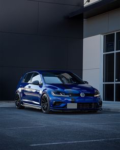 a blue volkswagen golf gtr parked in front of a large building with black windows