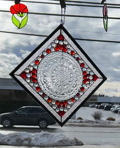 a stained glass sun catcher hanging in front of a building with cars parked on the street