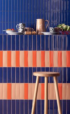 a wooden stool in front of a blue tiled wall with orange and pink tiles on it