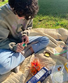 a person sitting on a blanket with food and drinks in front of them while holding a toothbrush