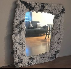 a mirror that is sitting on the floor in front of a wall with a couch behind it