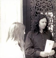 a man with long hair standing next to a woman in front of an iron door