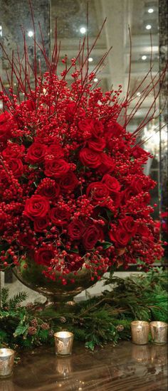 a vase filled with red roses and greenery on top of a table next to candles