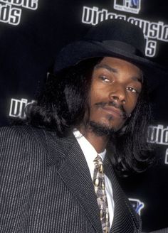 a man with long hair wearing a suit and tie in front of a microphone backdrop