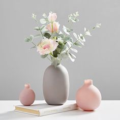 two vases with flowers in them sitting on a table next to a book and a candle