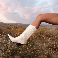 a woman's legs with white boots and flowers in the foreground at sunset