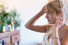 a woman wearing a birdcage veil while looking at her hair in the mirror