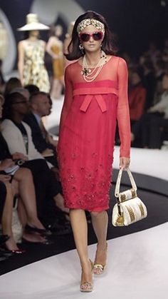 a woman is walking down the runway in a red dress and headpiece with pearls on it
