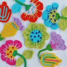 crocheted flowers are arranged on a white tablecloth with green stems and leaves