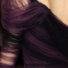 a woman wearing a purple dress with sheer fabric on the shoulders and neck, looking down at her cell phone