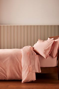 a bed with pink sheets and pillows on top of wooden flooring next to a striped wall