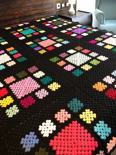 a crocheted bed with a black bedspread covered in multicolored hearts
