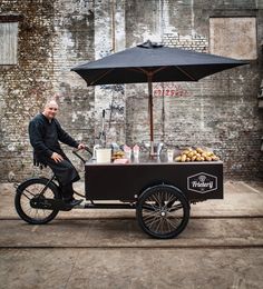 a man on a bike with an ice cream cart in front of him and an umbrella over his head